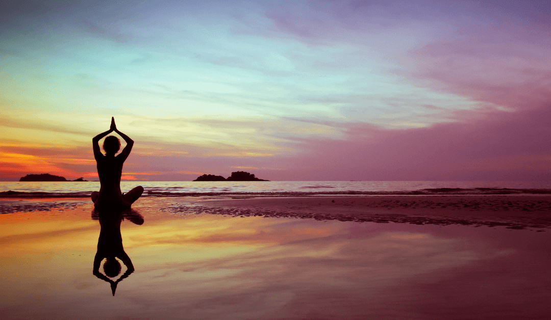 A woman doing yoga at the beach at sunset.