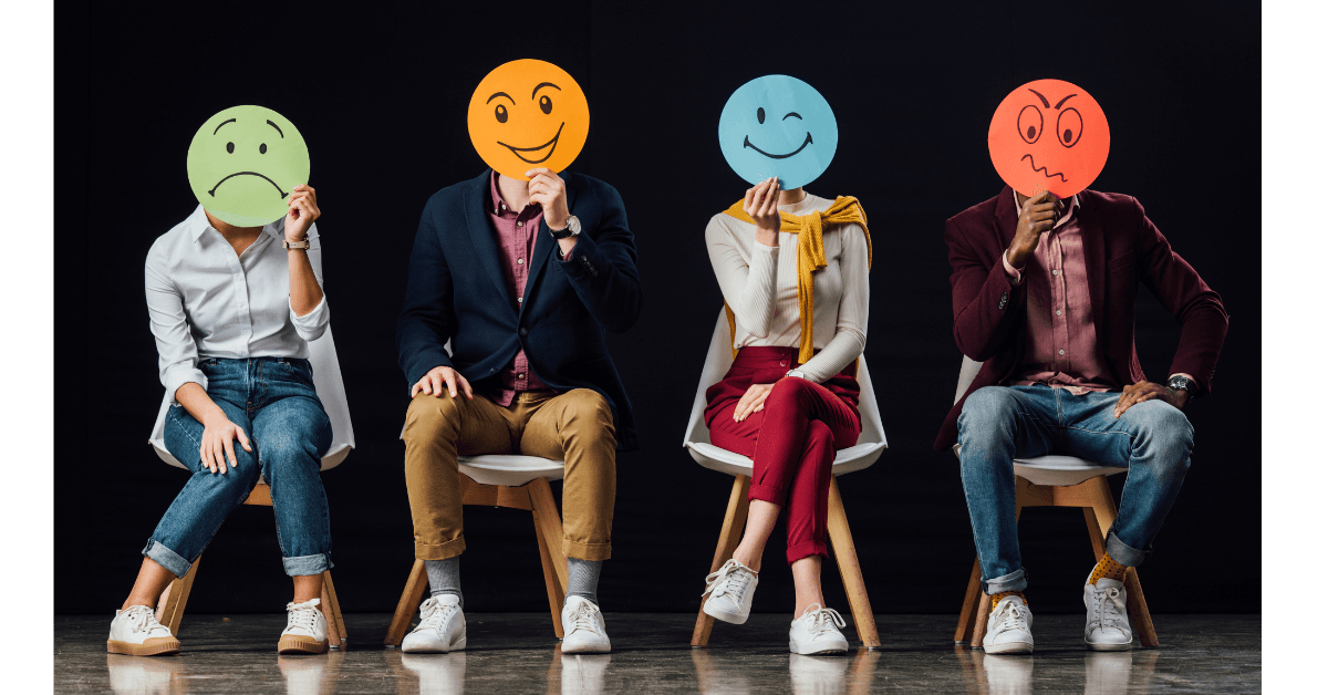 Four people sitting on chairs. Each holds a smily face with a different emotional expression in front of their face.