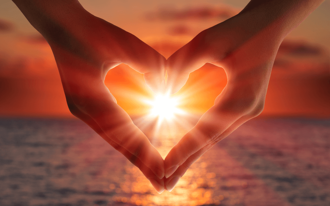 Two hands shape a heart around the setting sun. 