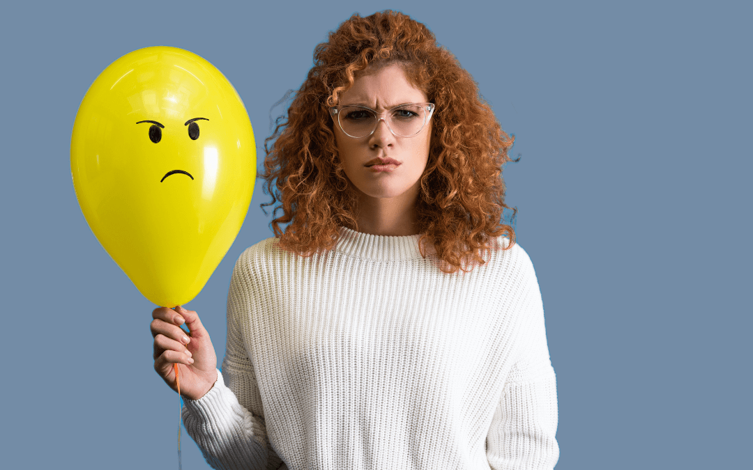 Non-plussed woman holding a balloon with an angry face drawn on it. 