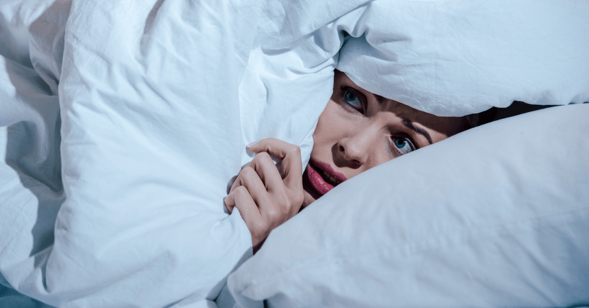 Woman hiding under covers in fear.
