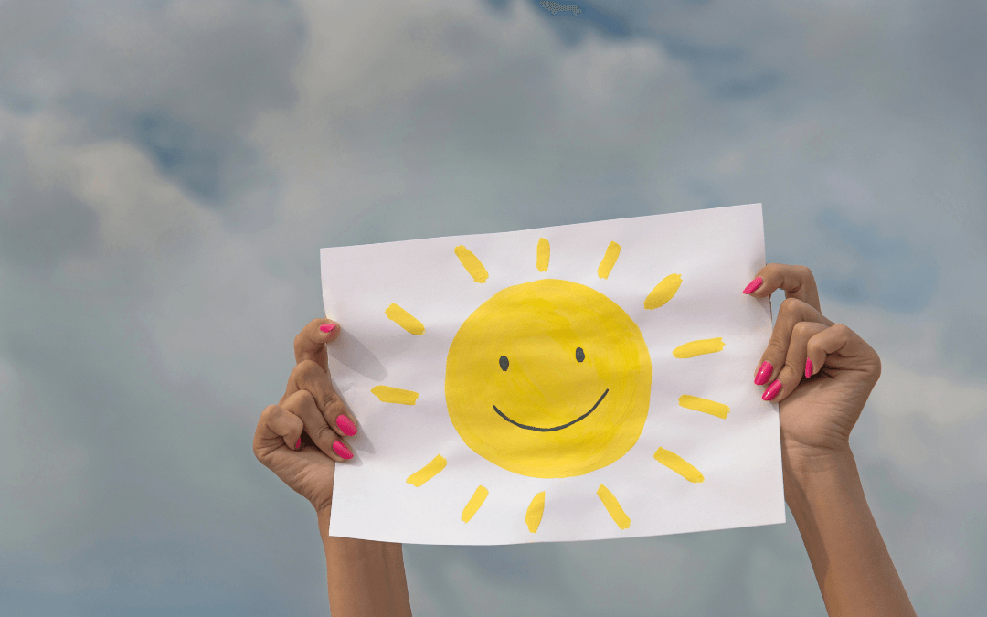 A woman holds up a paper with a smily sun on it. 