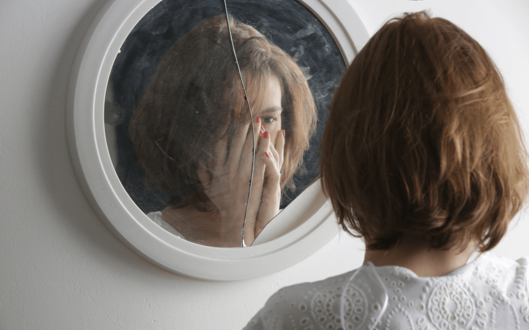 A woman looking at her reflection in a broken mirror.