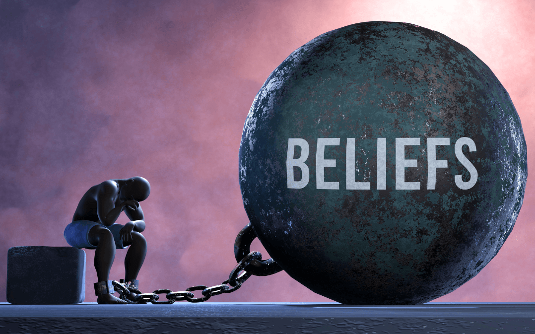 A man has a giant iron ball with the word beliefs chained to his ankle. It keeps him stuck in place. 