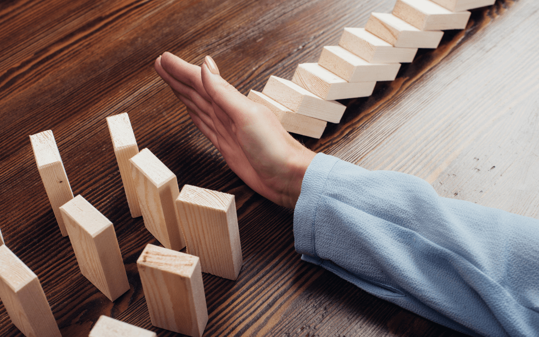 A hand stops a row of dominoes before it can topple over three more rows. 