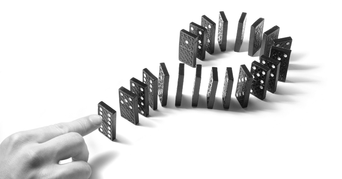 Dominoes placed in the shape of a question mark. A hand is about to push the first one over, starting a chain reaction. The image illustrates that worry is a system.